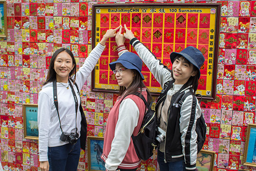International students pointing at the surname mural