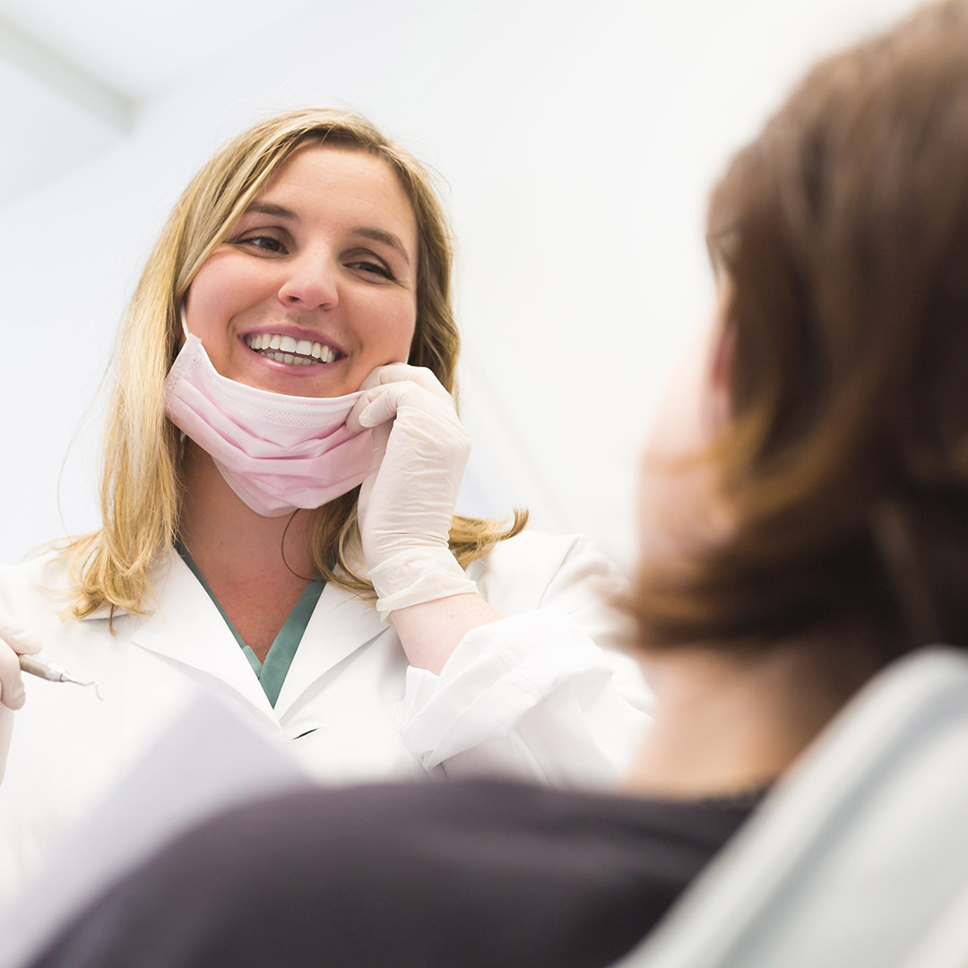 Dental assistant pulls down her mask and smiles at a patient