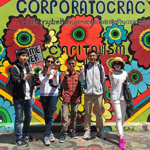 International students in front of a mural about corporatocracy