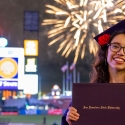 Graduate at Commencement holds up her diploma while fireworks explode at Giants stadium