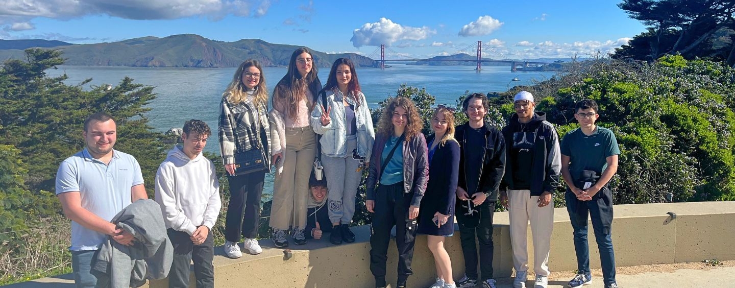 International students with water and the Golden Gate Bridge behind them and cute clouds over it