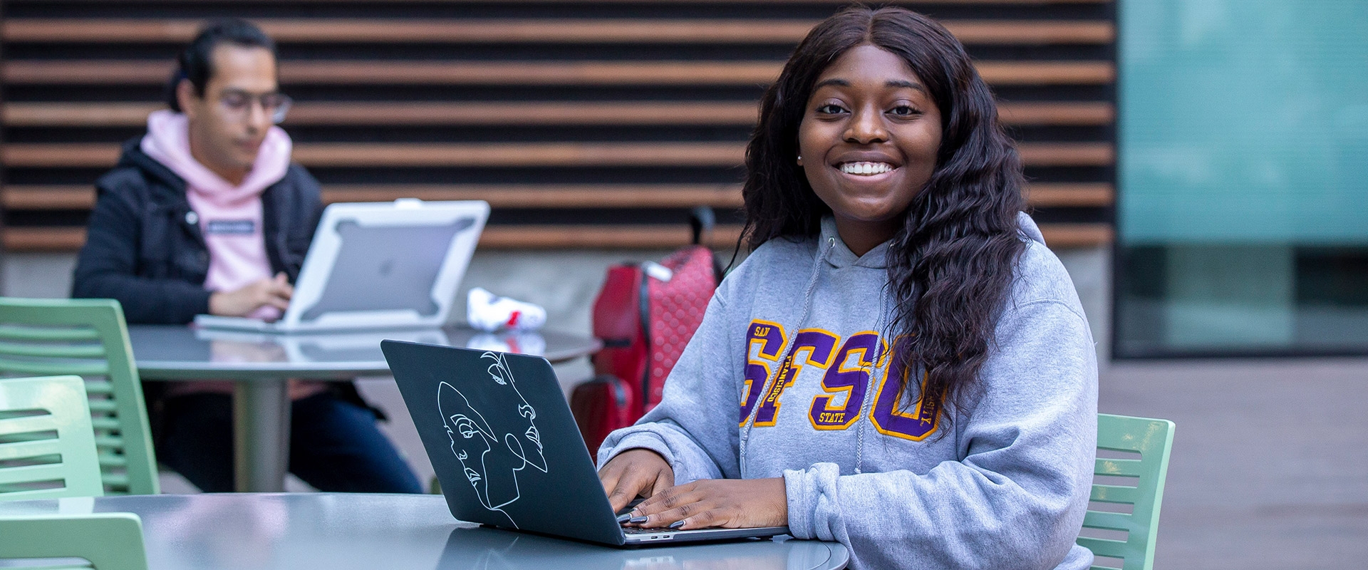 Woman in an SFSU sweatshirt taking a GE online course outdoors