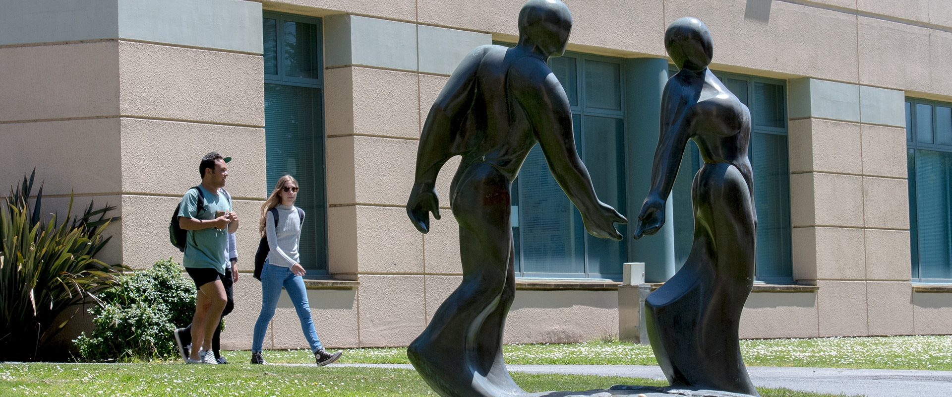 Couple walks on campus in the background of a couple sculpture