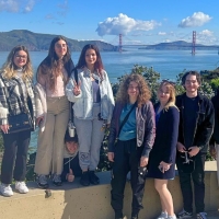 International students with water and the Golden Gate Bridge behind them and cute clouds over it