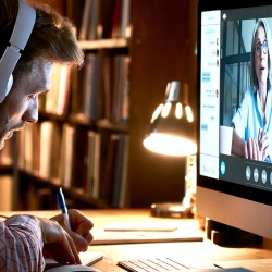 Man takes online course at a desk, while wearing headphones